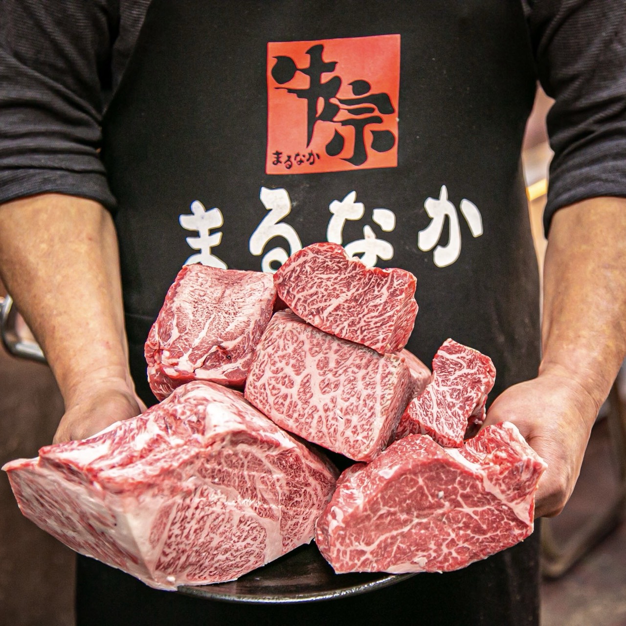 「牛宗 まるなか」のエプロン姿で黒毛和牛を抱える様子
